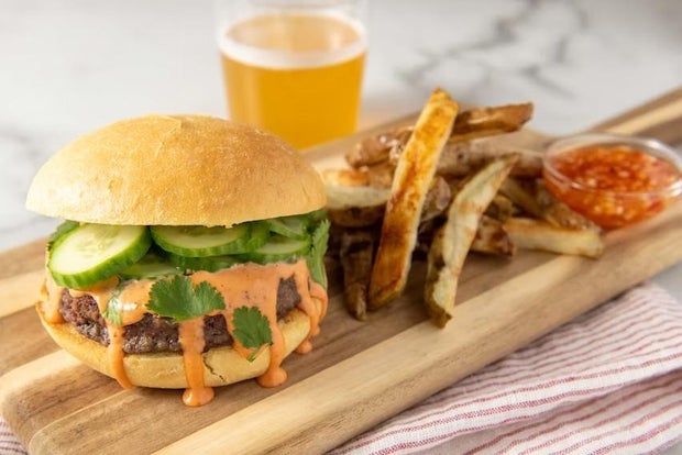 Impossible banh mi burger with sweet chili garlic fries, prepared on a cutting board with chili garlic sauce