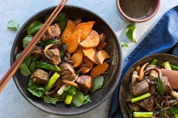 Vietnamese shaking beef split between two bowls with chopsticks next to a bowl of watercress and lime-pepper dipping sauce