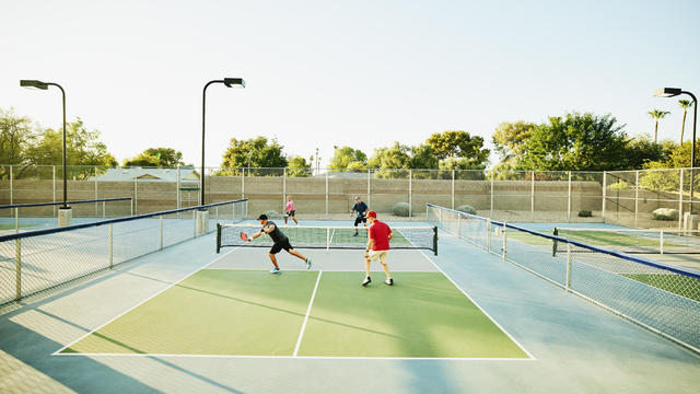 Extreme wide shot of senior friends playing doubles pickleball on sunny summer evening 