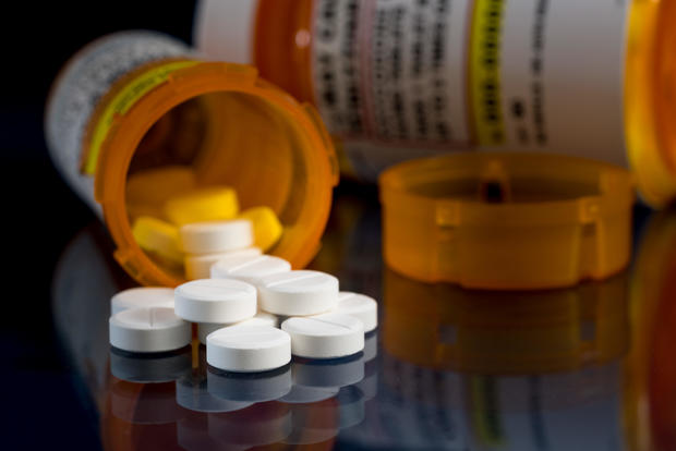 Macro of oxycodone opioid tablets with prescription bottles against dark background 