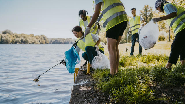Young female and male environmentalist cleaning lake while picking plastic from claw 