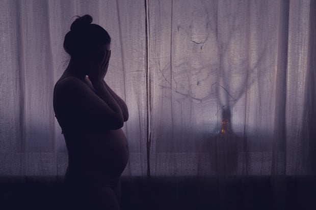 Young pregnant woman crying with her hands folded near her face. Pregnancy problems, silhouette of the expectant mother at the night window 