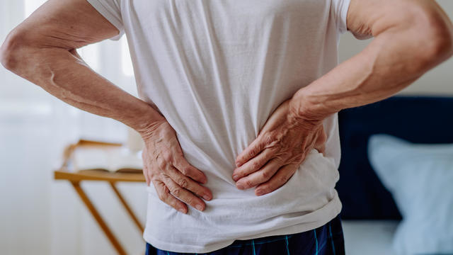 Senior man having back pain, standing in his bedroom. 