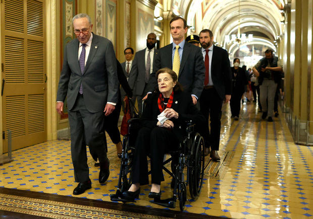 Senate Majority Leader Charles Schumer escorts Sen. Dianne Feinstein as she arrives at the U.S. Capitol following a long absence due to health issues on May 10, 2023. 
