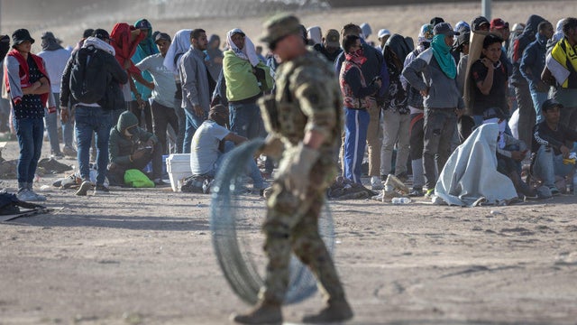 Immigrants watch as a Texas National Guard soldier prepares to uncoil razor wire around a makeshift immigrant camp located between the Rio Grande and the U.S.-Mexico border fence on May 10, 2023 in El Paso, Texas. 