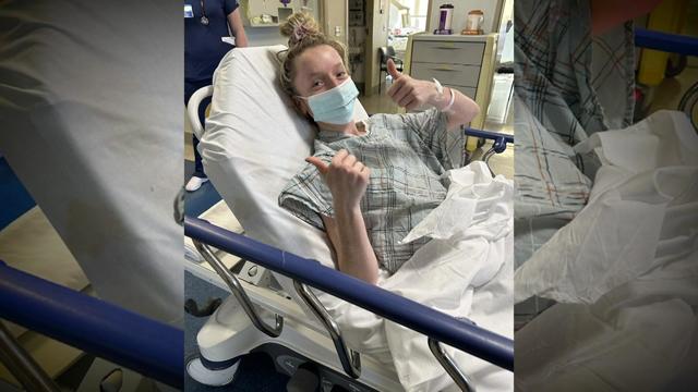 Taylor Everson gives two thumbs up to a camera while lying in a hospital bed. 