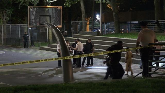 Police officers search a basketball court blocked off by crime scene tape. 