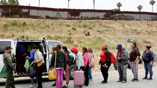 A U.S. Border Patrol agent keeps watch as immigrants enter a vehicle to be transported from a makeshift camp between the U.S. and Mexico on May 13, 2023, in San Diego, California. 