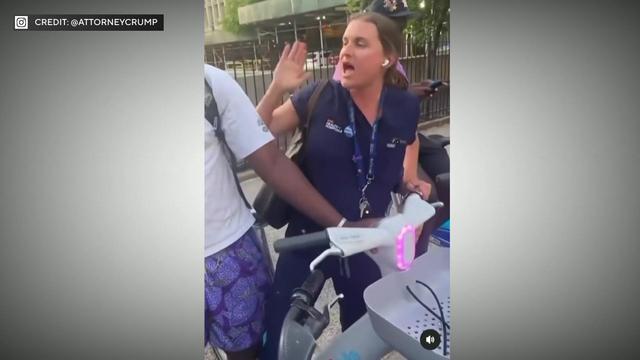 A white woman in NYC Health + Hospital scrubs holds onto a Citi Bike that a Black man is also holding. 