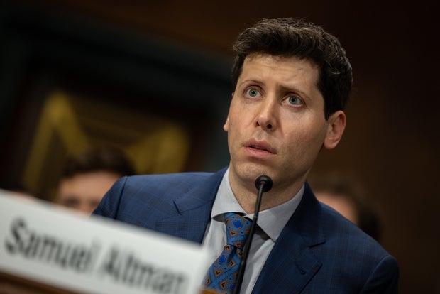 Sam Altman behind a mic in blue suit