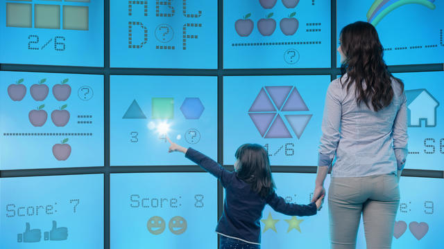 Mother and daughter standing in front of graphical screens showing educational images, girl reaching out to touch screen 
