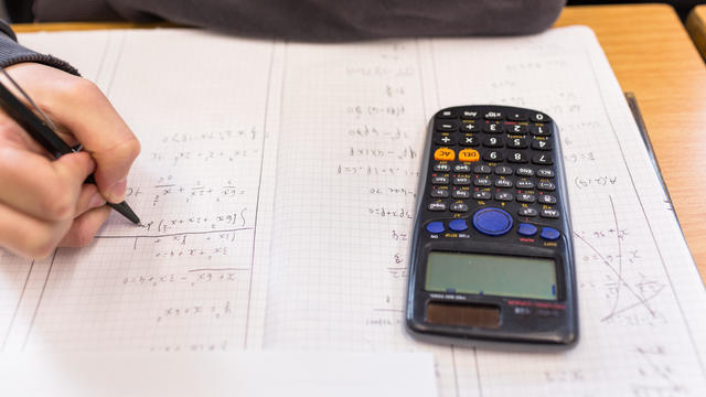 Person solving math equations on paper with calculator 