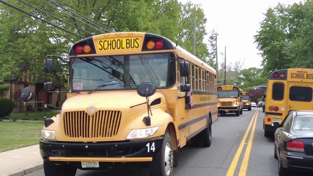 Multiple school buses drive down a residential road. 