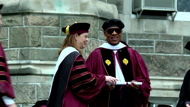 A Fordham University official hands Stevie Wonder a diploma at commencement. 