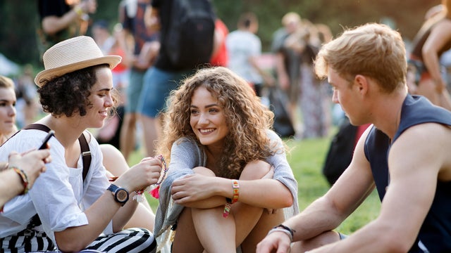 Group of young friends sitting on ground at summer festival. 