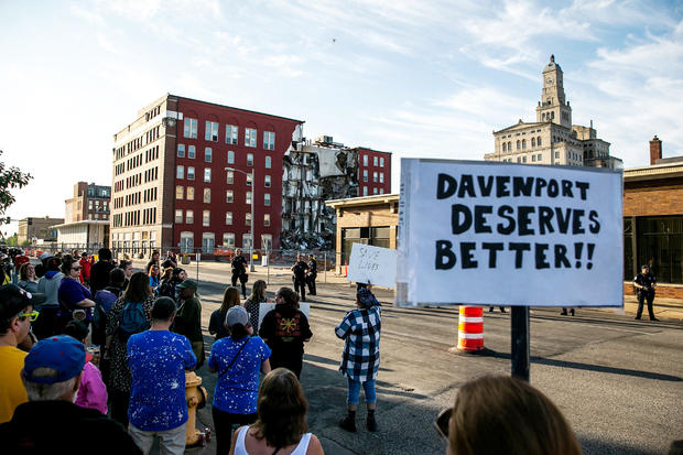 Davenport police officers form a line opposite protesters near apartment building that partially collapsed in Davenport 