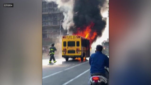 Flames engulf a school bus on a street. 