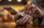 Closeup image of a man holding and using smart phone with coffee cup on wooden table in cafe 