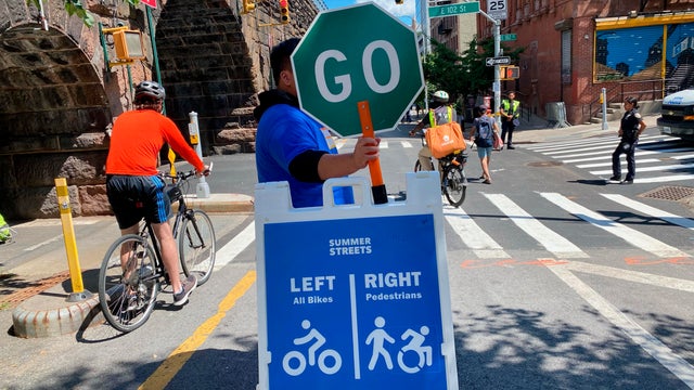 Summer Streets event traffic volunteer holding Go sign and cyclists, Manhattan, New York City 