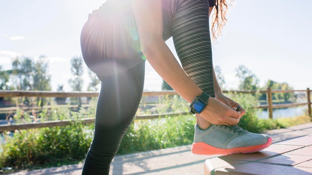 Woman with one foot up on a bench, tying her shoe before workout