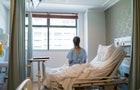 Female patient sitting on bed in hospital ward 