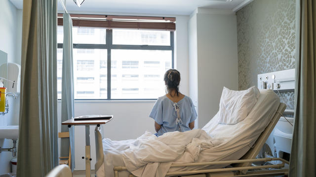 Female patient sitting on bed in hospital ward 