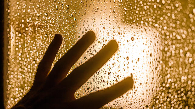 Depression and goodbye concept: dark silhouette of human hand on window with rain drops 