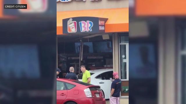 A white sedan sits partially inside a Dunkin' Donuts after apparently crashing through the storefront. 