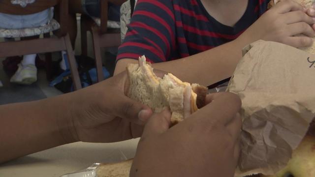 A child holds a sandwich included in a brown bag lunch. 