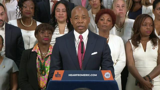 New York City Mayor Eric Adams stands behind a podium in front of members of the New York City Council 