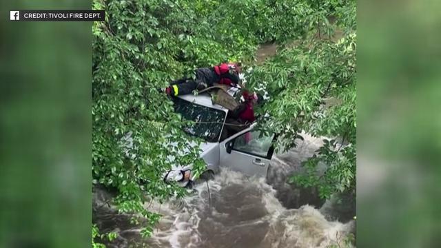 First responders lay on the roof of a silver vehicle sitting in the middle of a stream. 