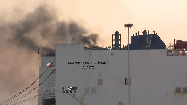 Flames and smoke can be seen rising from a large ship in Port Newark. 