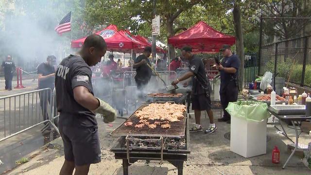 FDNY members cook on grills in the street at a block party. FDNY popup tents are in the background. 