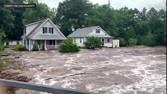 Brown floodwaters surround two homes. 