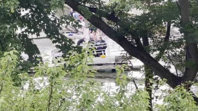 Through trees, EMS responders can be seen surrounding someone on a boat ramp. 