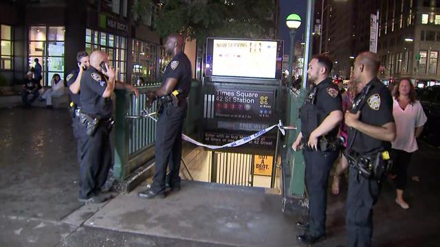 Five NYPD officers stand outside an entrance to the Times Square subway station that is blocked off by police tape. 