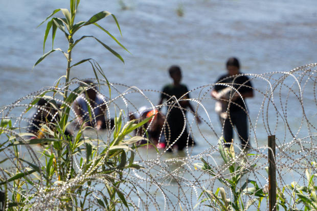 Migrants walk behind Concertina wire in the water along the Rio Grande border with Mexico in Eagle Pass, Texas, on July 15, 2023. 