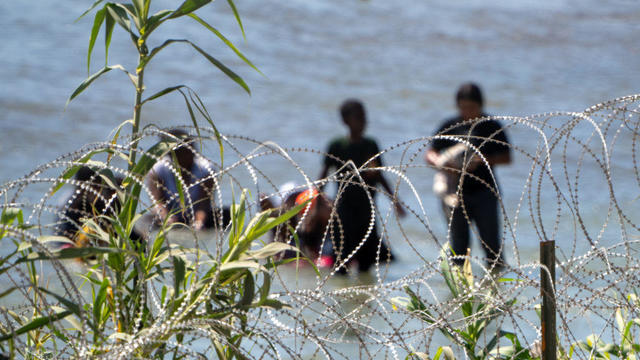 Migrants walk behind Concertina wire in the water along the Rio Grande border with Mexico in Eagle Pass, Texas, on July 15, 2023. 