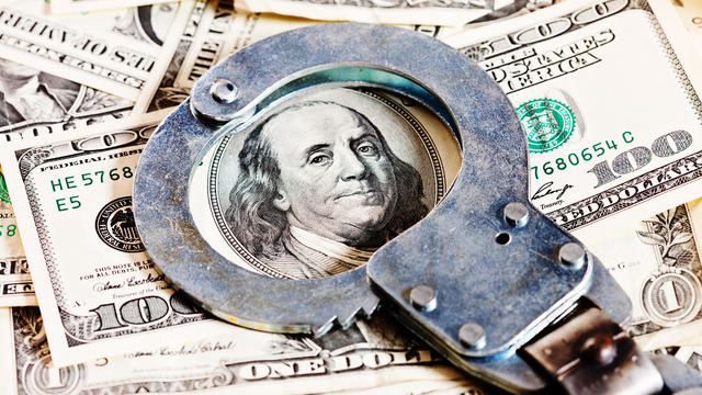 Handcuffs circle Benjamin Franklin in stack of dollars 