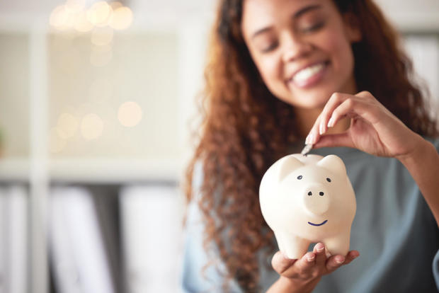 A happy young mixed race woman is holding a piggybank and depositing a coin as savings  Hispanic woman budgeting her finances and investing money for her future.  Saving funds for financial independence 