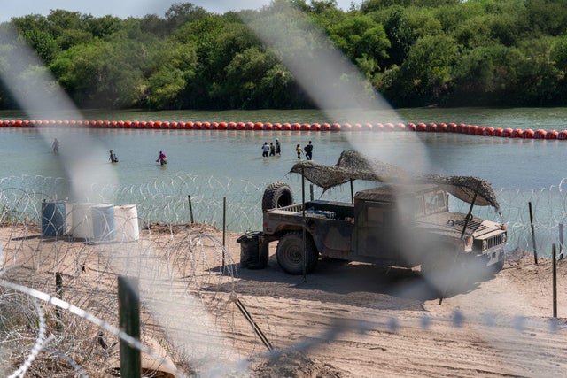 Migrants walk by a string of buoys placed on the water along the Rio Grande border with Mexico in Eagle Pass, Texas, on July 15, 2023, to prevent illegal immigration entry to the U.S.
