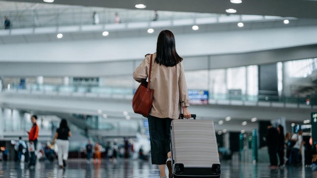 Rear view of young Asian woman carrying suitcase walking in airport terminal. Ready to travel. Travel and vacation concept. Business person on business trip 