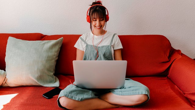 Woman with headphones working on laptop in living room