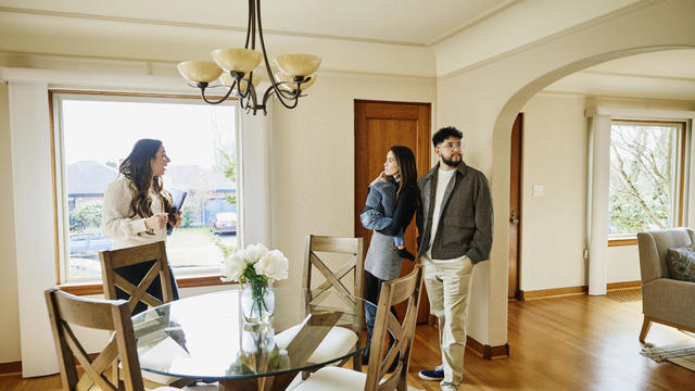 Wide shot of family looking at home for sale with real estate agent 