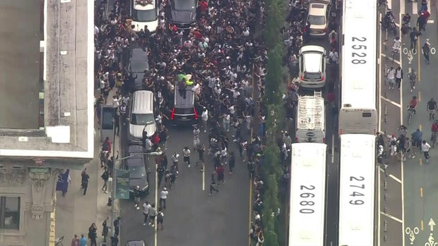 An aerial view of hundreds of people swarming an SUV as it tries to leave the Union Square area. A passenger looks out the moon roof.