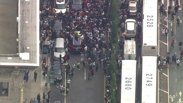 An aerial view of hundreds of people swarming an SUV as it tries to leave the Union Square area. A passenger looks out the moon roof. 