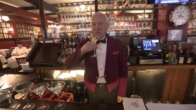 Joe Petrsoric stands behind the bar at Sardi's holding a martini. 