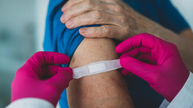 Doctor wearing gloves puts a Band-Aid on a woman's arm after vaccination shot 