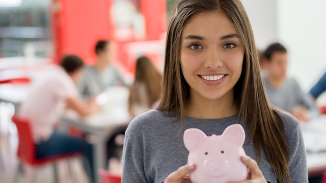 Beautiful female student at the library holding a piggy bank looking at camera smiling 