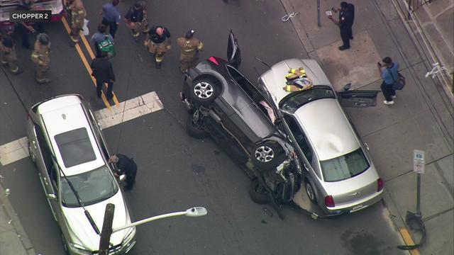 An aerial view of a car crash on a seat in Jersey City. A dark gray vehicle lays on its driver's side next to a parked silver sedan. 